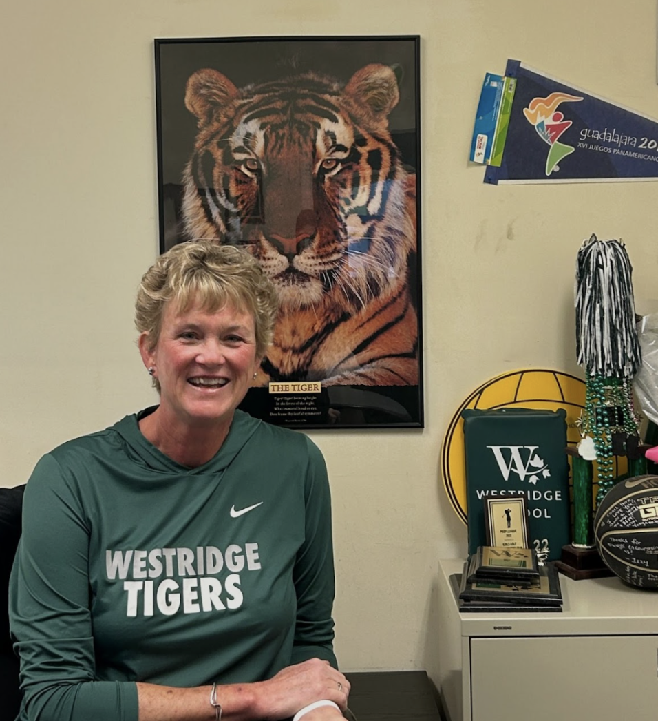 Coach Horn sits in front of a cluster of sporting trophies and an inspirational tiger poster.  
(Gemma A. '27)